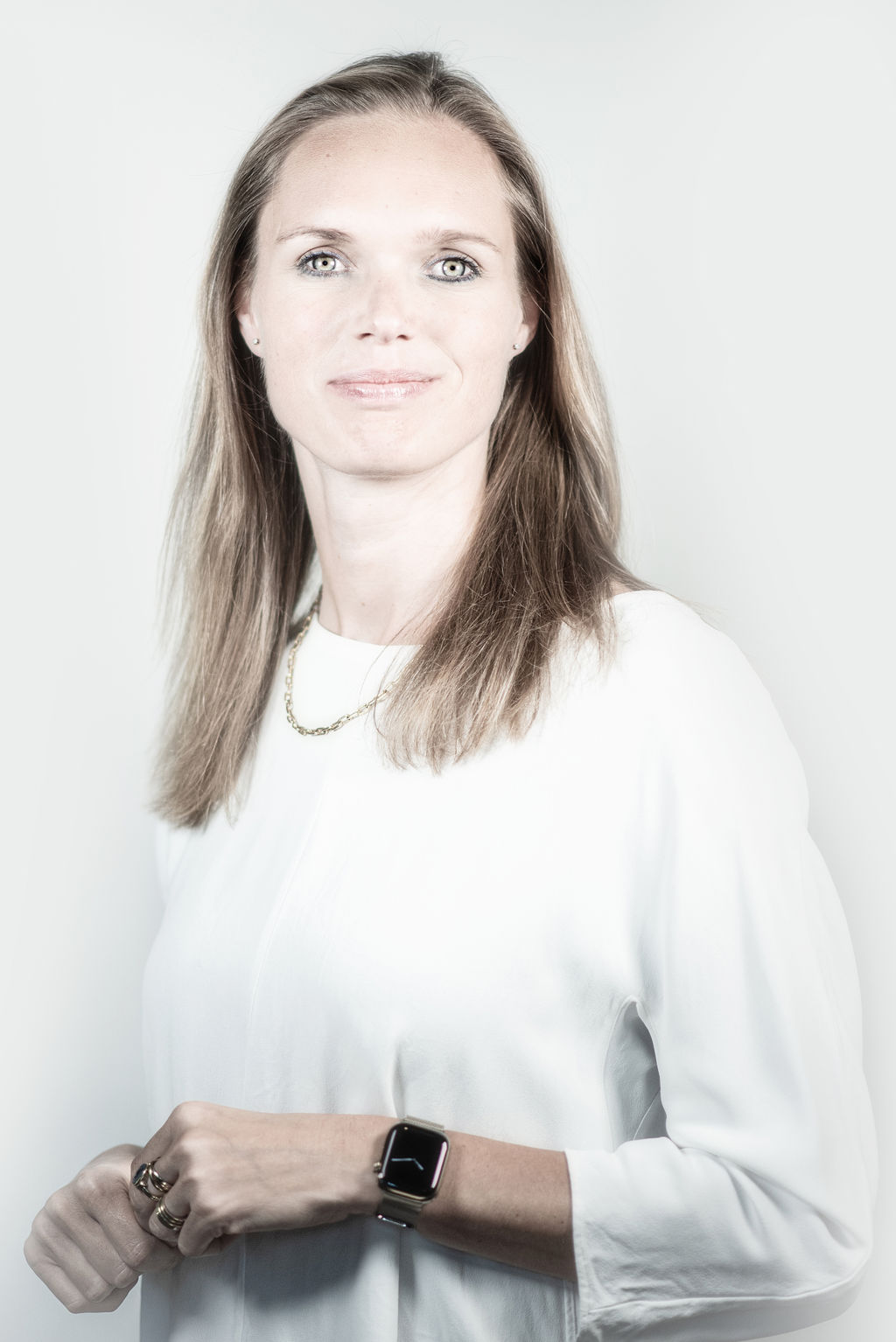 Portretfoto: Tjarda lacht met opengesloten mond. Zij staat voor een witte achtergrond. Zij draagt wit shirt met driekwartmouw, heeft een zwarte horloge aan en ringen om haar linker ring- en middelvinger.